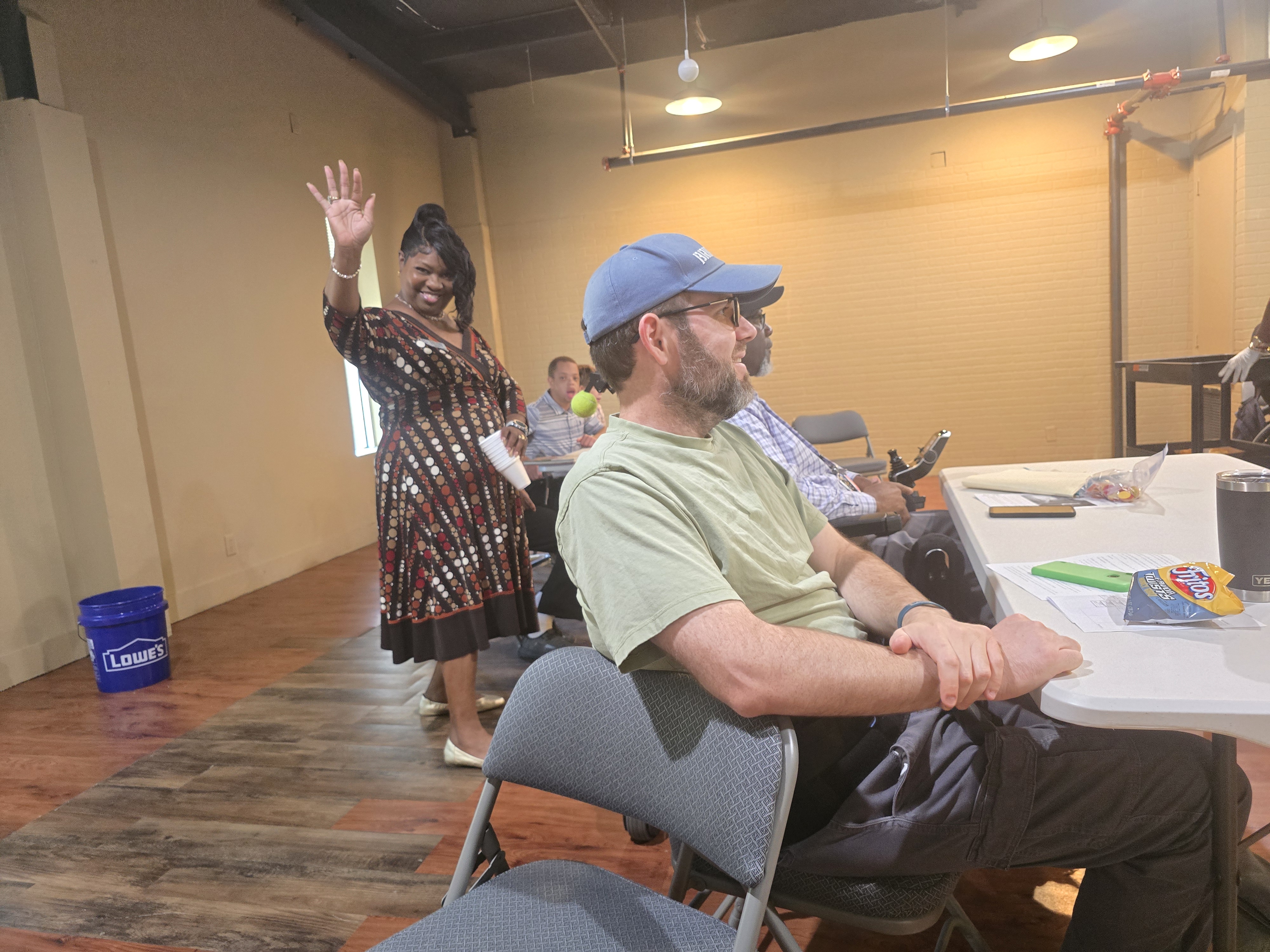 Lesia Dailey waving with Jared seated in the same shot during the September 2026 Spinal Cord Injury Support Group meeting in Mobile, Alabama.