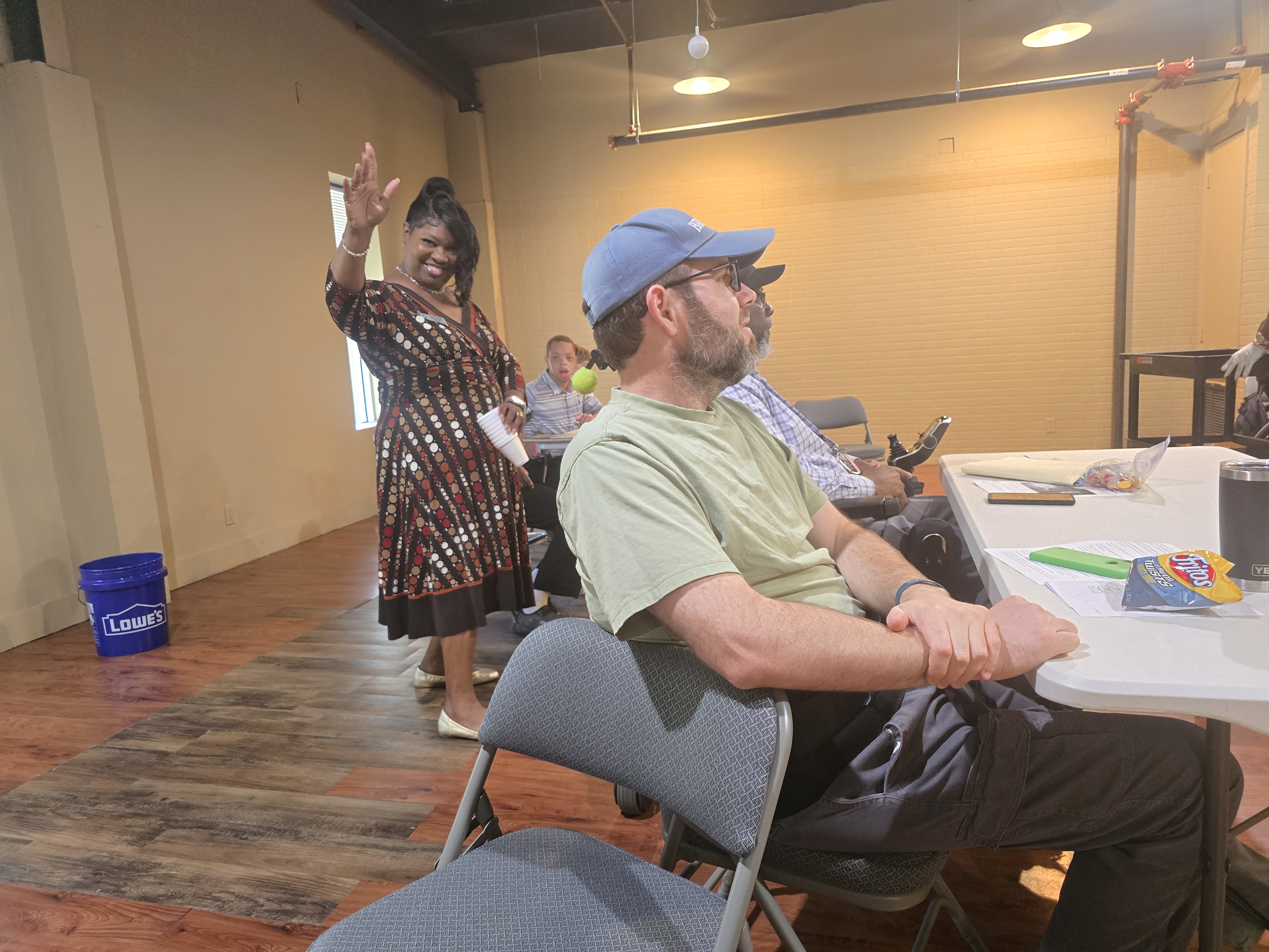 Lesia Dailey smiling and waving with Jared seated in the same shot during the September 2026 Spinal Cord Injury Support Group meeting in Mobile, Alabama.
